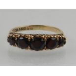 A 9 carat yellow gold and garnet ring, set five round cut graduated garnets.