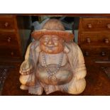 A South East Asian carved wooden figurine of a seated Buddha wearing a hat. H.40cm