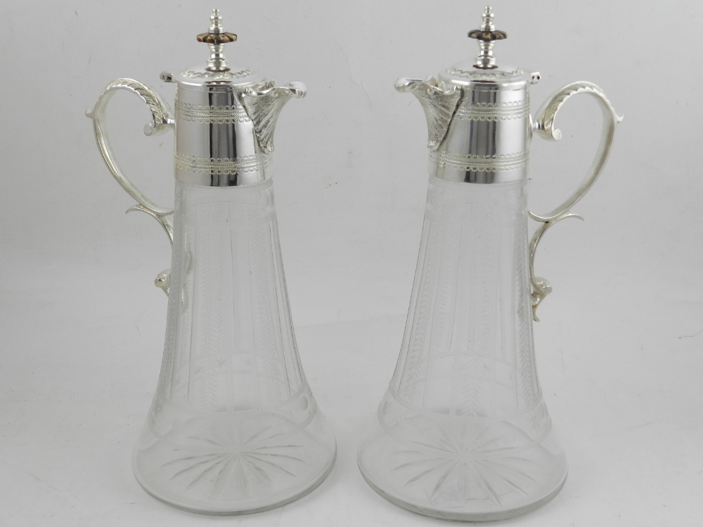 A pair of cut glass claret jugs, having silver plate handles and lids. H.30cm