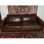 A Contemporary brown leather three seater sofa, raised on cast metal supports.