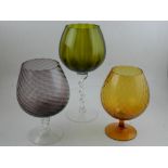 A group of three oversized glass wine goblets, of various colours.