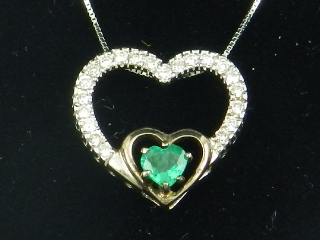 A white gold, diamond and emerald set heart-shaped pendant, suspended on a white gold chain.