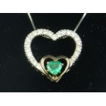 A white gold, diamond and emerald set heart-shaped pendant, suspended on a white gold chain.