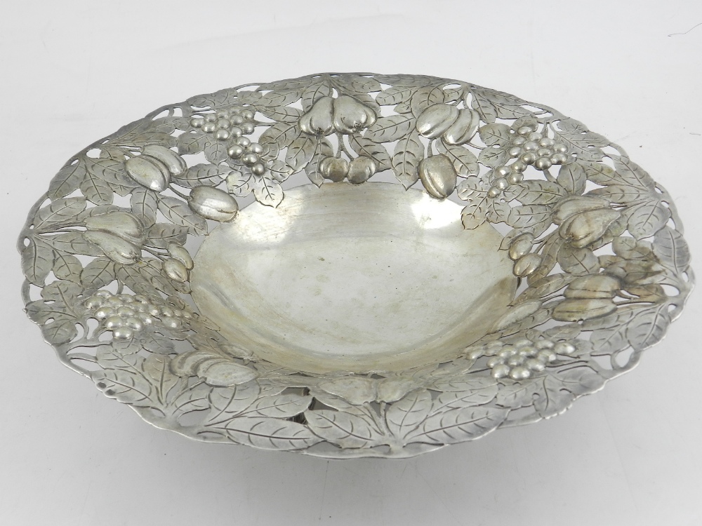A Continental white metal dish, the pierced edge repousse decorated with fruit, raised on