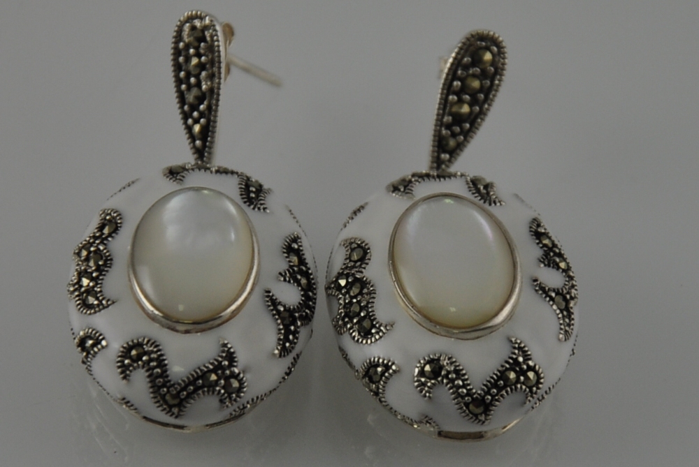 A pair of silver and white enamel earrings with a marcasite and mother of pearl centre