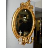 A 19th century giltwood girandole oval mirror, having elaborately carved crest top and bottom. H.