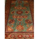 A green ground Kazak rug, having geometric patterned centre, within stylised flower borders,