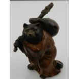 A cold painted bronze study of a bear wearing a robe and carrying a bindle.