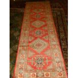 A red ground Kazak runner, having three lozenge medallions to centre, within floral borders,