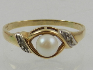 A 9 carat yellow gold and pearl crossover style ring, the shoulders set with diamond accents.