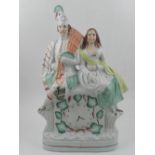A 19th century Staffordshire figural study of a Scottish man and woman sitting on a clock. H: 38cm
