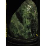 A large polished green jade specimen on a wooden base, H.