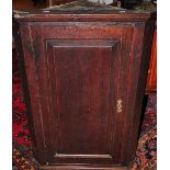 An early 19th century oak hanging corner cabinet enclosed by a panelled door,