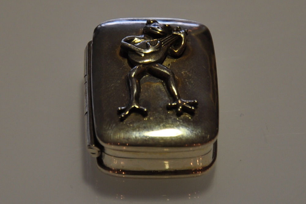 A rectangular silver box with a frog playing a guitar on the lid