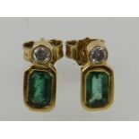 A pair of yellow gold, diamond, and emerald stud earrings.