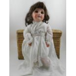 An early 20th century porcelain doll, in a white cotton dress, together with a small wicker picnic