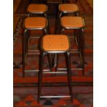 A set of five chrome tubular bar stools, having orange seats.
