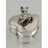A novelty silver heart-shaped pill box, the lid surmounted with a cat.