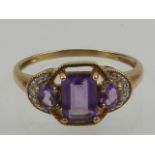 A yellow gold and amethyst three stone ring, the mount set with diamond accents.