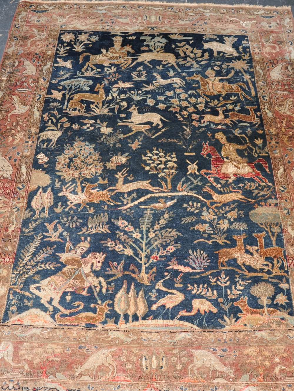 A Qum handmade wool carpet,decorated with a Shekari hunting scene on a dark blue ground,