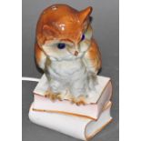 A child's glazed ceramic bedside lamp, modelled as an owl, with blue glass eyes, perched upon books,