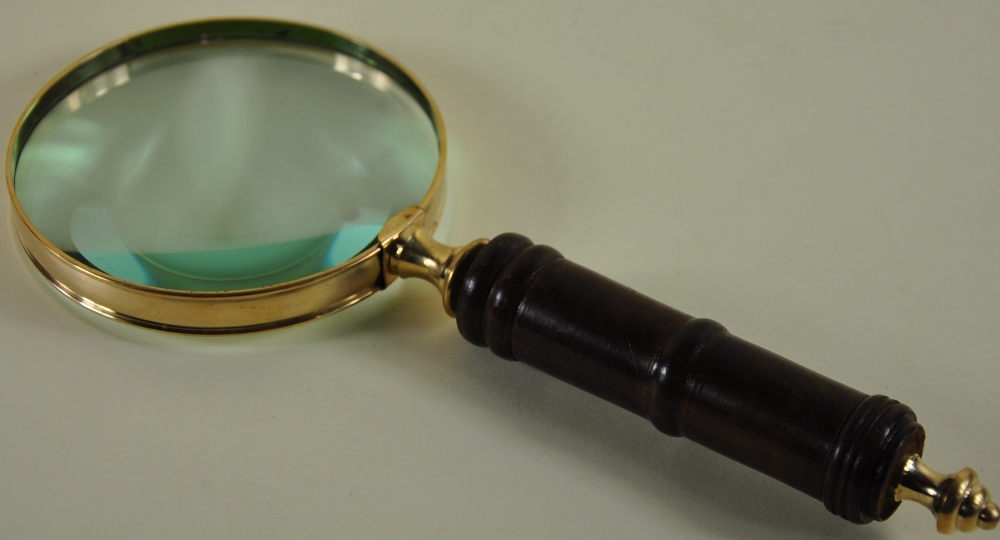 A large brass table magnifier with a wooden handle