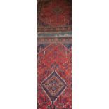 A pair of Shiraz brick red ground rugs woven central hooked lozenge medallions within a dense