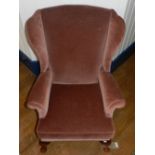 A Parker Knoll wing-back arm chair, having pink upholstery, raised on wooden legs.