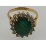A yellow metal, diamond, and emerald cluster ring, set large oval cut central emerald.