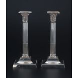 Paire de chandeliers en métal argenté en forme de colonne corinthienne. Fût cannelé et base carrée à