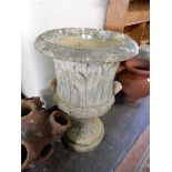 A large stone garden urn with leaf decoration, fitted twin handles, on circular leaf decorated base