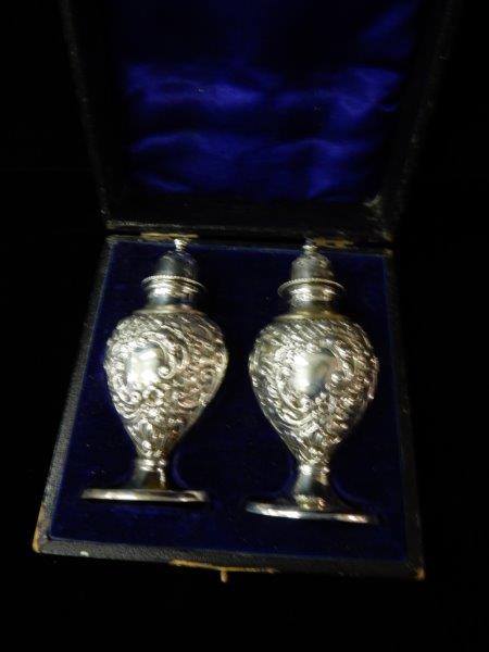 A pair of silver ovoid form pepper and salt pots with repousse decoration of flowers and leaves,