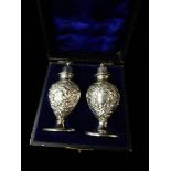 A pair of silver ovoid form pepper and salt pots with repousse decoration of flowers and leaves,