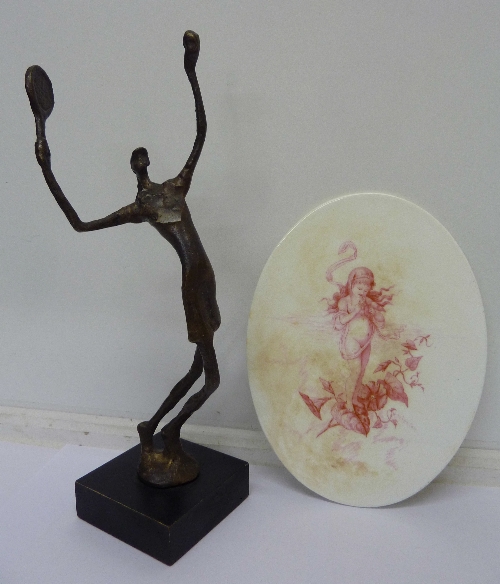 A stylised cast figure of a female tennis player and an oval plaque/stand