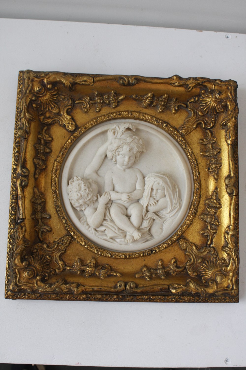 A marble style circular plaque depicting a cherub group, framed with an ornate gilt frame,