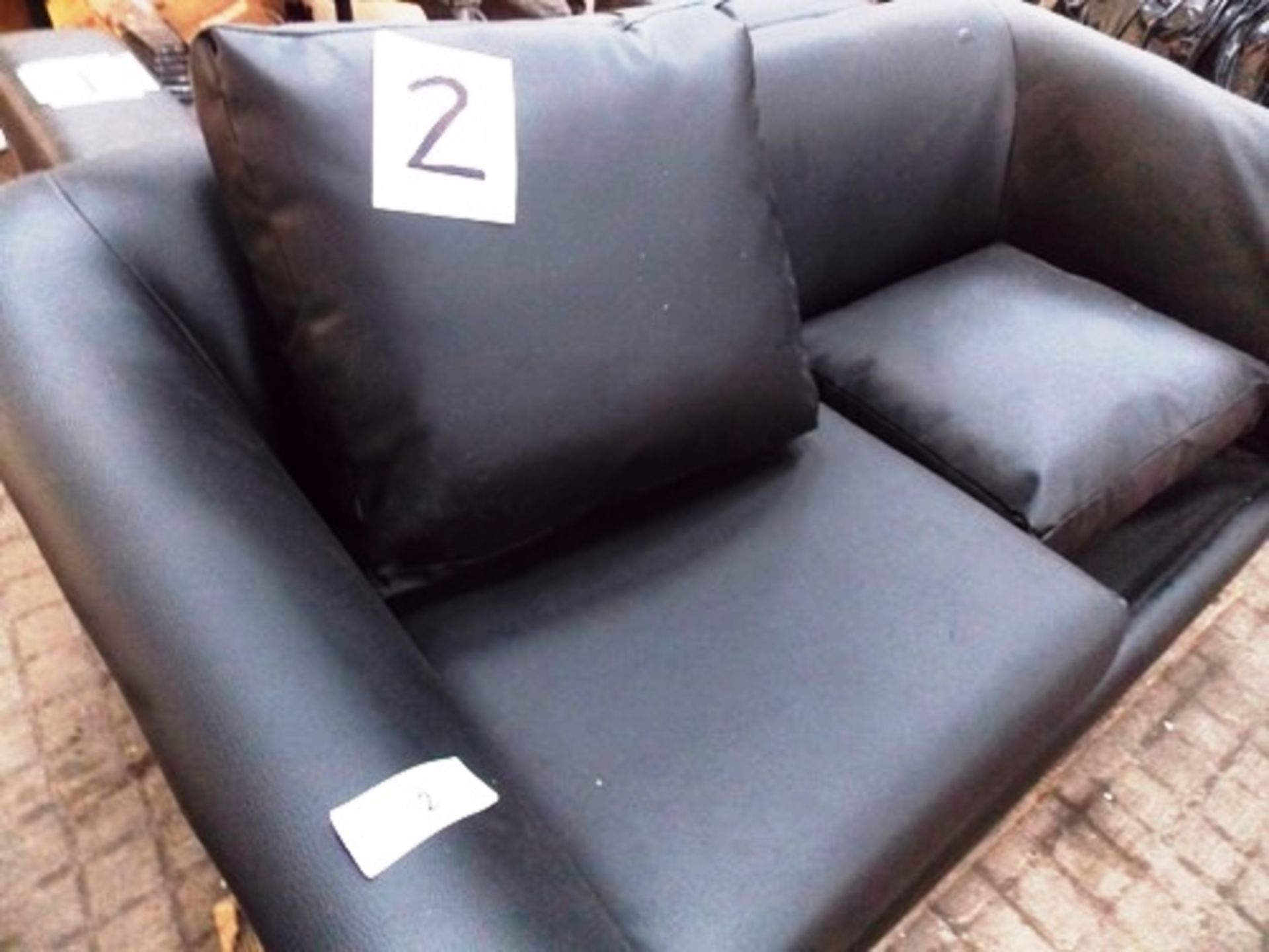An unbranded 2 seater sofa, finished in black faux leather, missing 1 cushion, with broken armrest