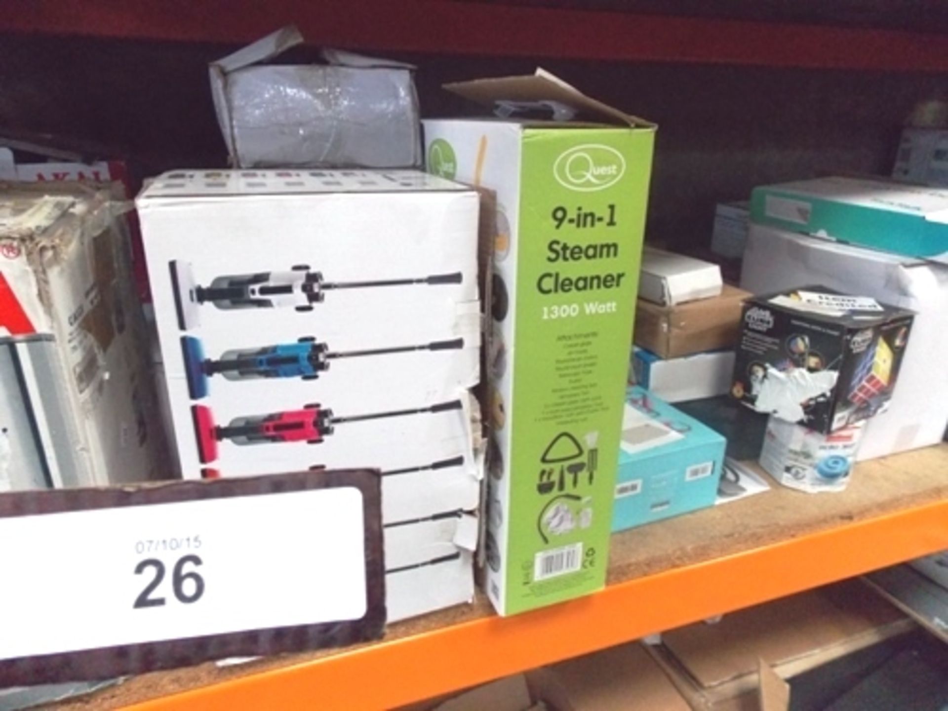 A shelf of mixed electrical and cleaning items including vacuum cleaners, steam cleaners, hand