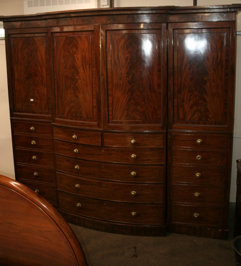 An early 19th Century mahogany bow fronted breakfront wardrobe, surmounted by a stepped cornice,