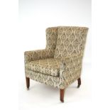 An Edwardian upholstered wing back armchair, raised on square tapering supports,