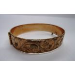 A 9ct gold bangle with cut leaf scroll d