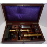 A brass monocular microscope on iron horseshoe base with lenses in fitted mahogany case. Further