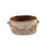An early 19th Century salt glazed pie dish with ploughing scene decoration and lion masks