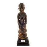 An ethnic wooden carving of a seated female with Cowrie shell decoration,