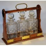 An Edwardian oak three bottle tantalus, of typical form with brass 'C' scroll carrying handle and