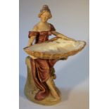 A late 19thC Royal Dux figure, of a lady seated holding a large shell, polychrome decorated in