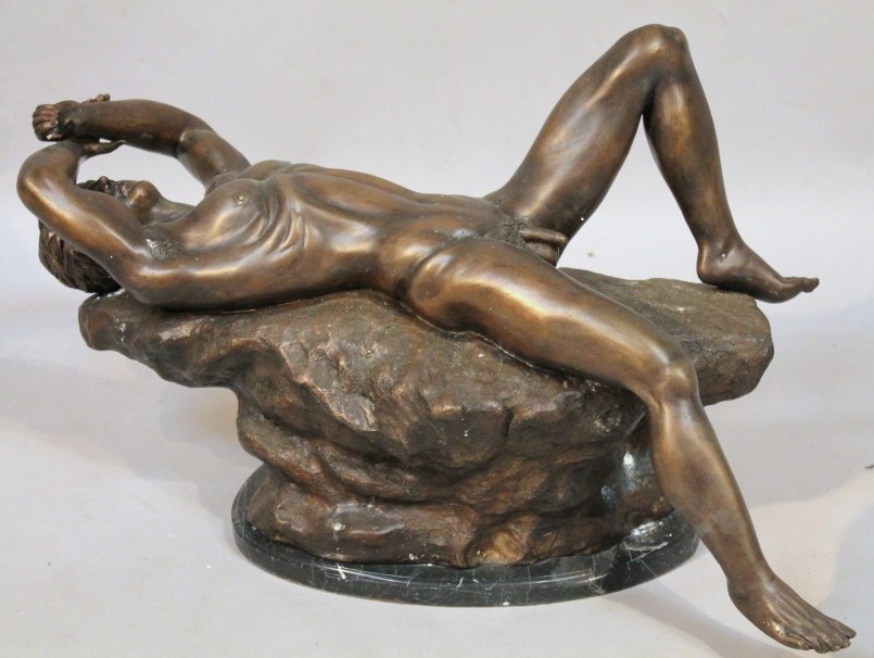 A bronzed figure, of a reclining nude male on a naturalistic rock work base and a textured marbled