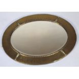 An early 20thC brass mirror, of oval form, with a hammered outline in a bell flower border broken by