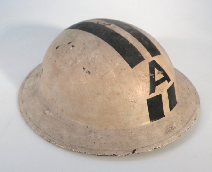 A tin helmet, painted cream with leather interior and canvas strap set with the letter A, 18cm