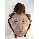 A Gabon African tribal mask, the carved wooden central face, with feathered and shell head dress,