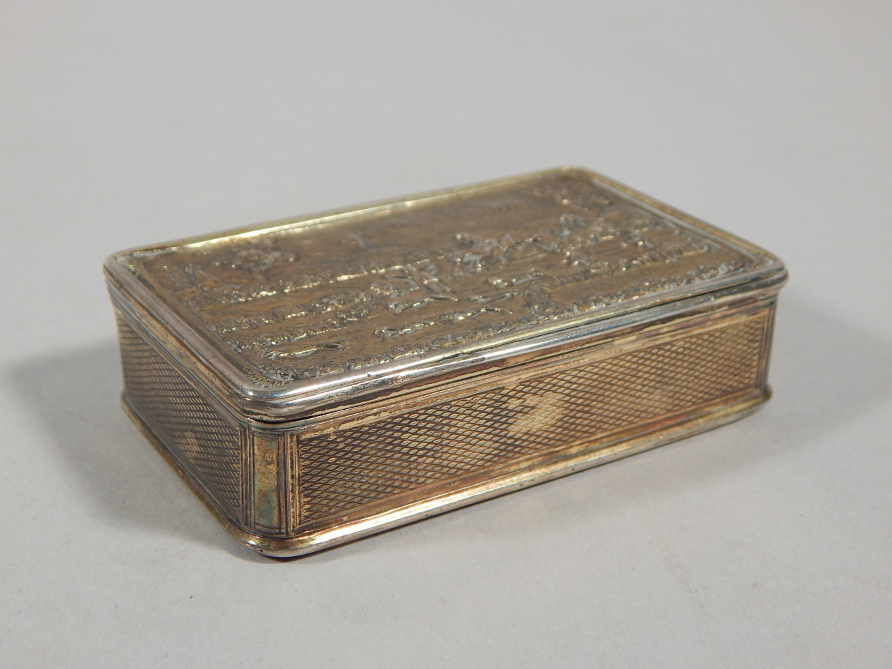 A George IV silver gilt snuff box, the hinged lid decorated with a hunting scene of figures on